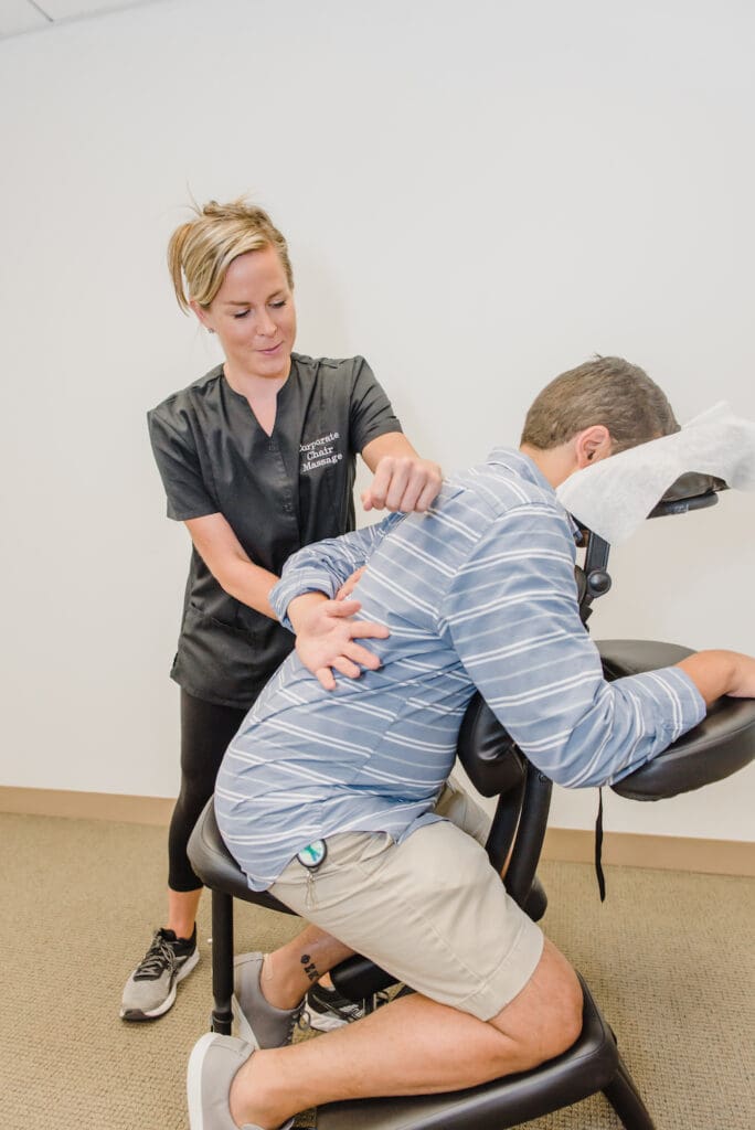 Corporate Chair Massages' owner Jeannette Sweeney stretches the left arm of a male customer behind his back to target the rhomboid muscle.