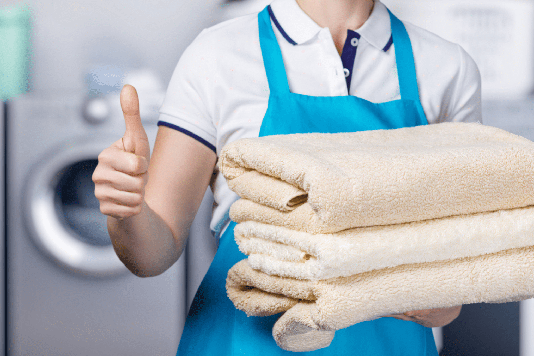 Housekeeper holds three folded towels in one hand while the other gives a thumbs up